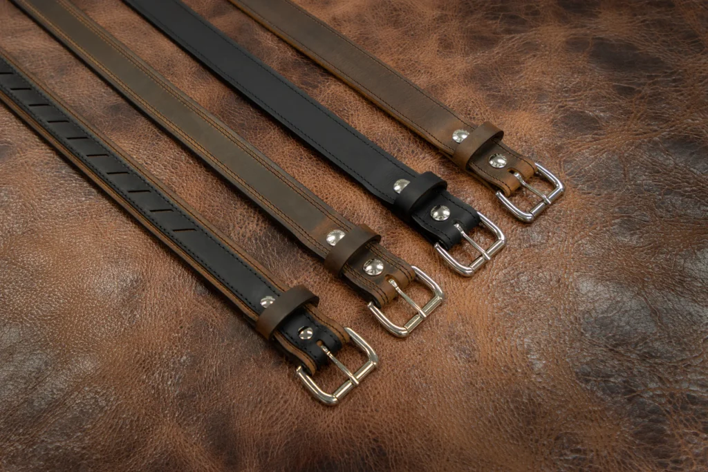 Finished leather belts with metal buckles laid out on a leather surface