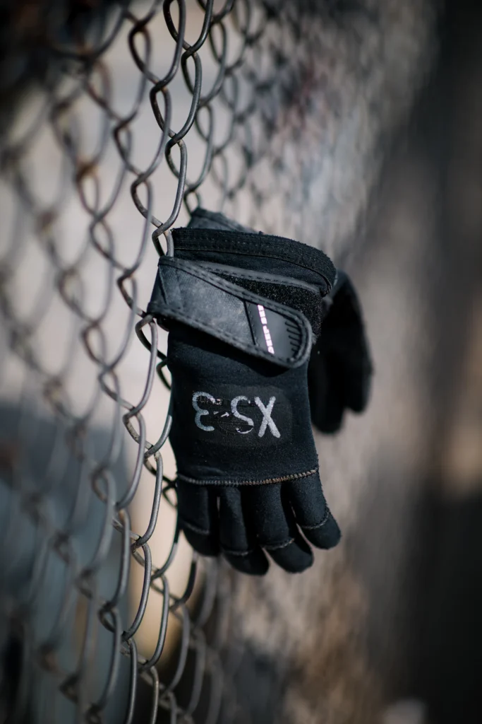 Full-finger training glove with wrist strap hanging on a wire fence
