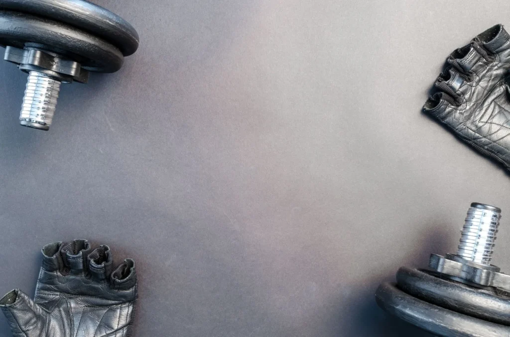 Flat lay of leather gym gloves and dumbbells on a grey surface