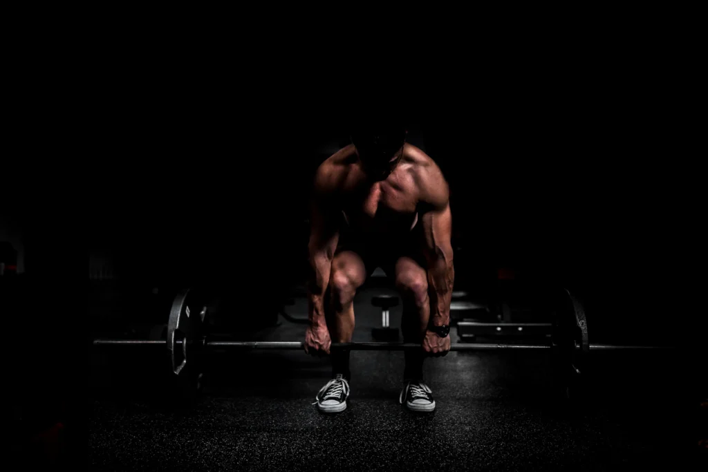 Athlete setting up a deadlift with a loaded barbell in a dark gym