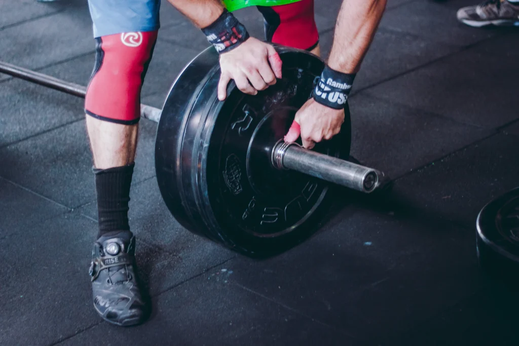 Lifter in knee sleeves and wrist wraps loading a barbell