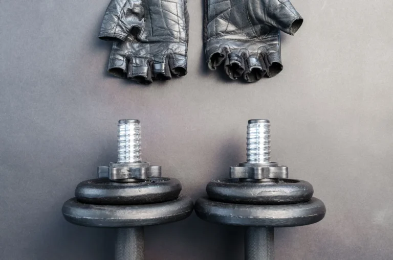 Pair of leather fingerless gym gloves above two dumbbells